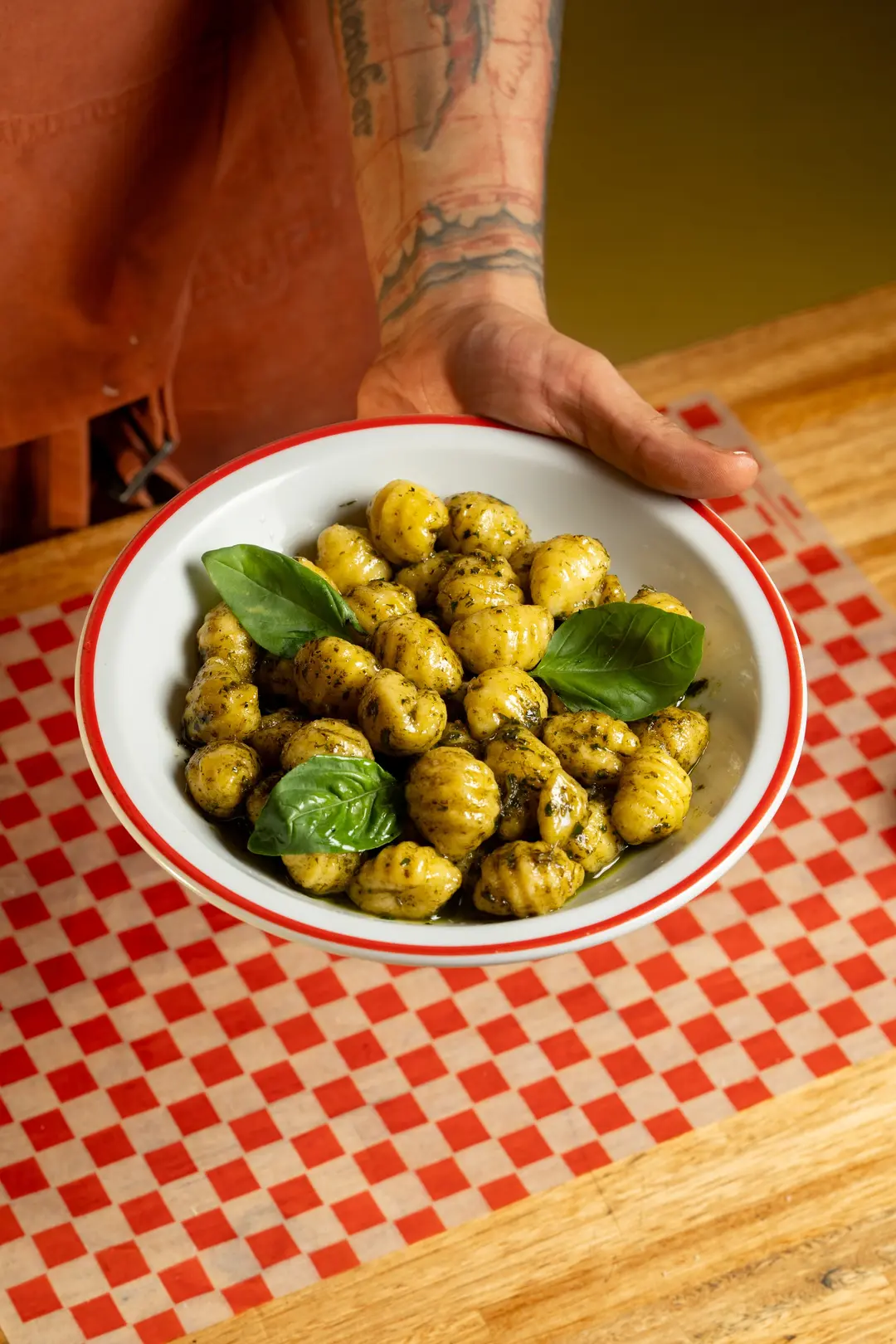 Manos apoyan en la mesa un plato de ñoquis con albahaca